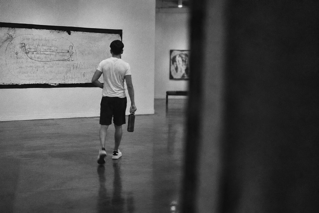 Eliezer de espaldas alejándose por una galería, visto desde detrás de una esquina